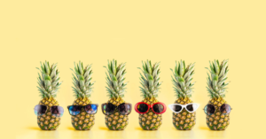 Six pineapples are stood up in a row with sunglasses put on each of the,.